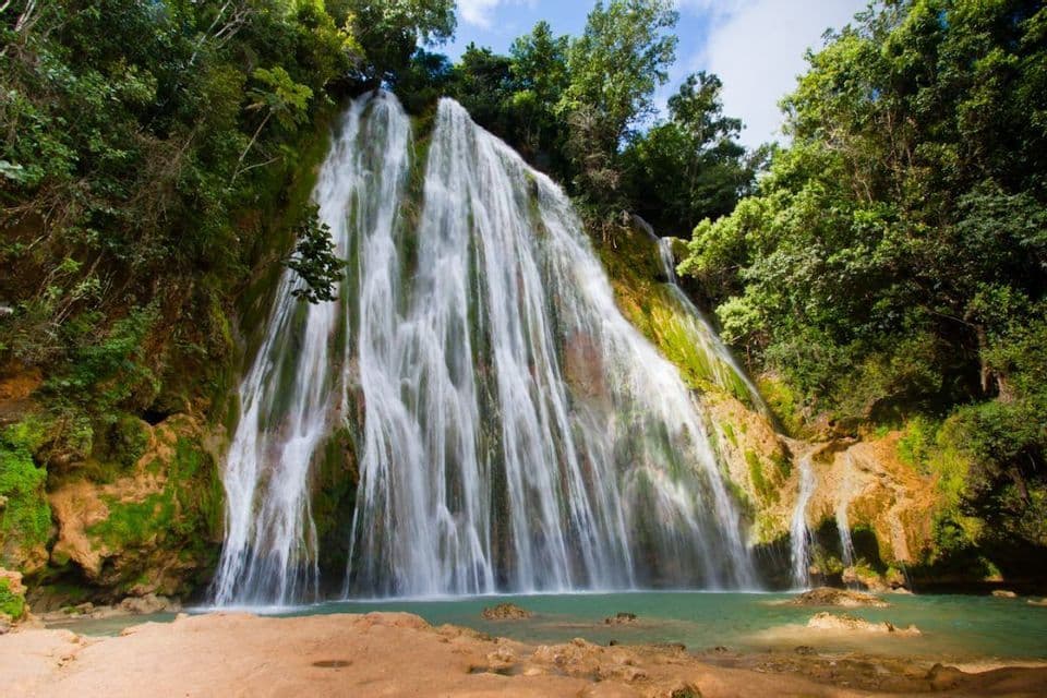Un'ampia cascata scende da una scogliera ricoperta di muschio in una pozza turchese in una giungla tropicale.