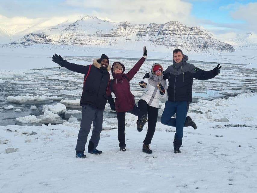 Un voyage de groupe WeRoad de quatre personnes posant dans un paysage enneigé avec un point d'eau gelé et des montagnes.