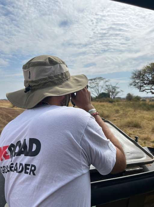 Un gearleader WeRoad con un cappello da safari guarda attraverso il binocolo da un veicolo scoperto nella savana.