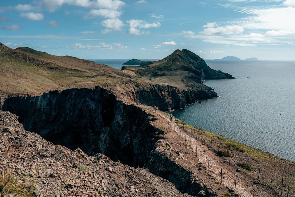 Eine WeRoad Gruppenreise: Wanderung auf einem schmalen Pfad entlang einer felsigen Küste, mit Blick auf das Meer und entfernte Inseln.