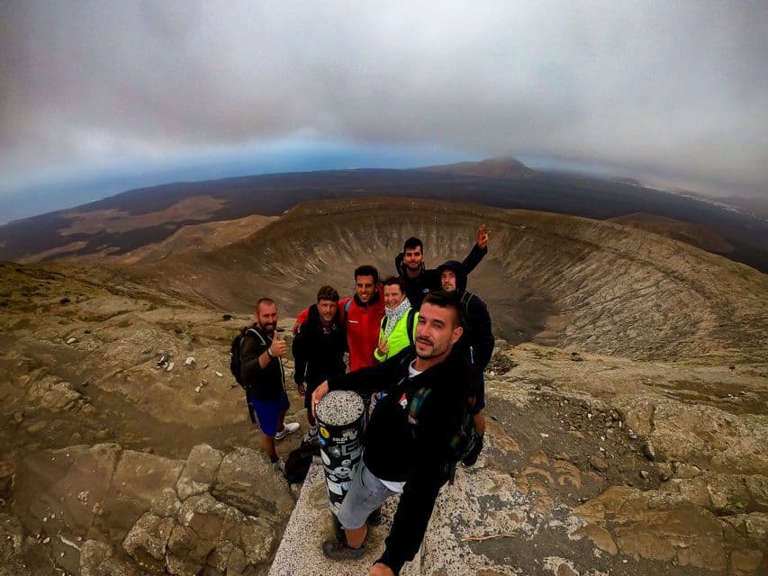 Un viaggio di gruppo WeRoad scatta un selfie sull'orlo di un cratere vulcanico sotto un cielo nuvoloso.