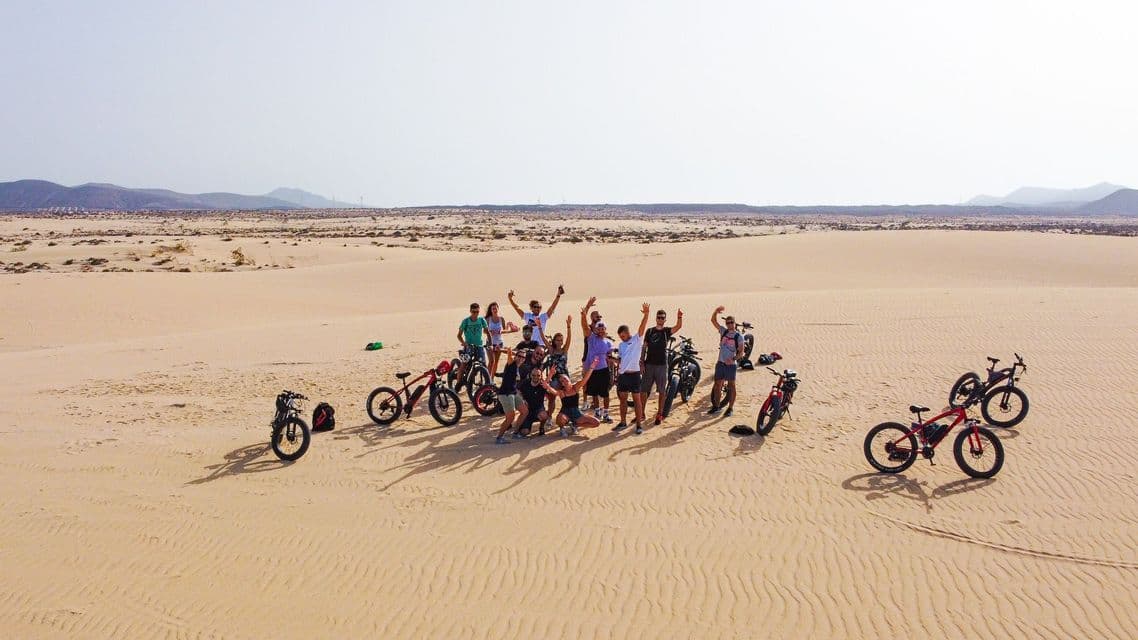 Un groupe WeRoad pose avec ses vélos à gros pneus sur des dunes de sable dans un paysage désertique.