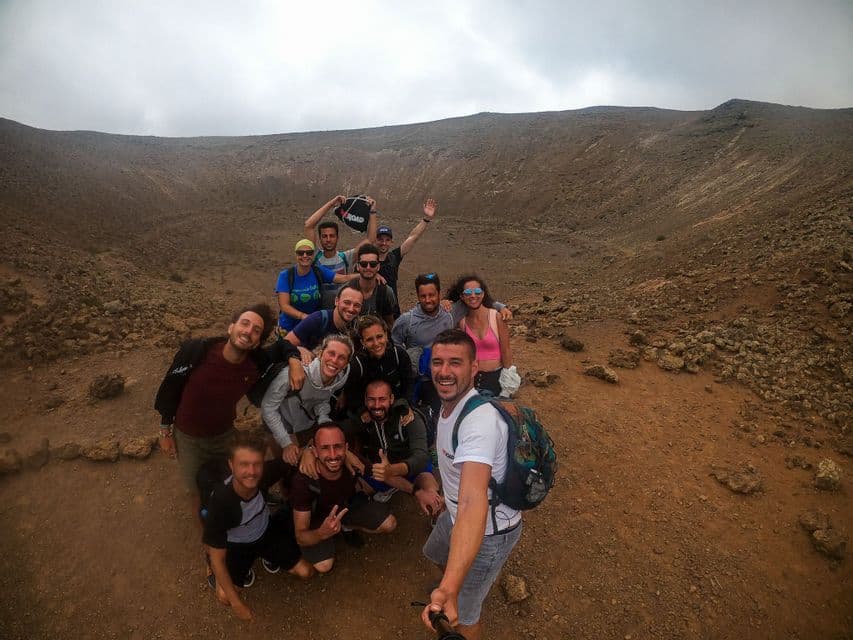 Un groupe WeRoad prend un selfie à l'intérieur d'un grand cratère volcanique rocheux sous un ciel couvert.