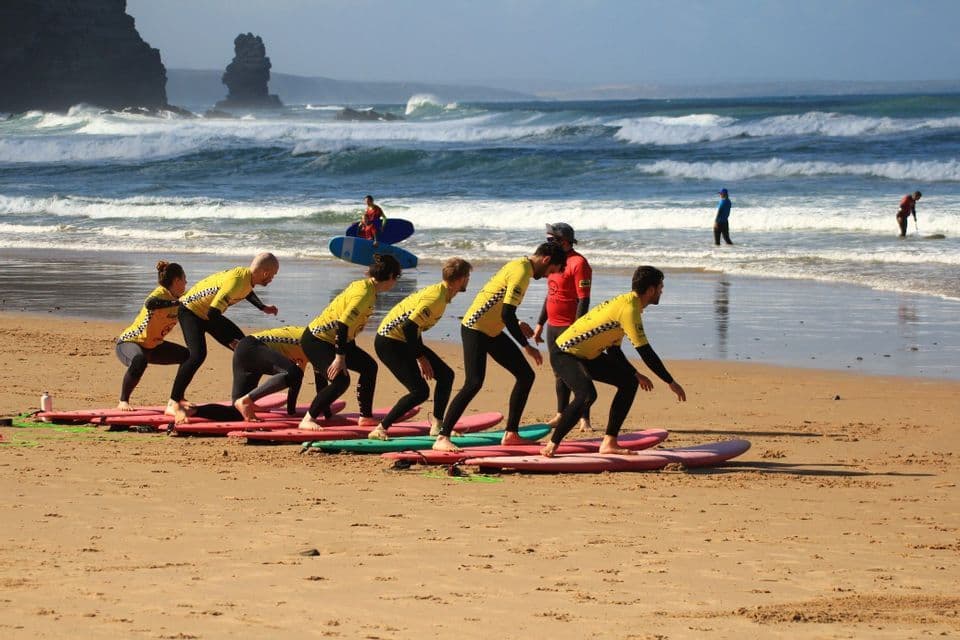 Un viaggio di gruppo WeRoad partecipa a una lezione di surf, imparando a stare in piedi sulle tavole da surf su una spiaggia sabbiosa.