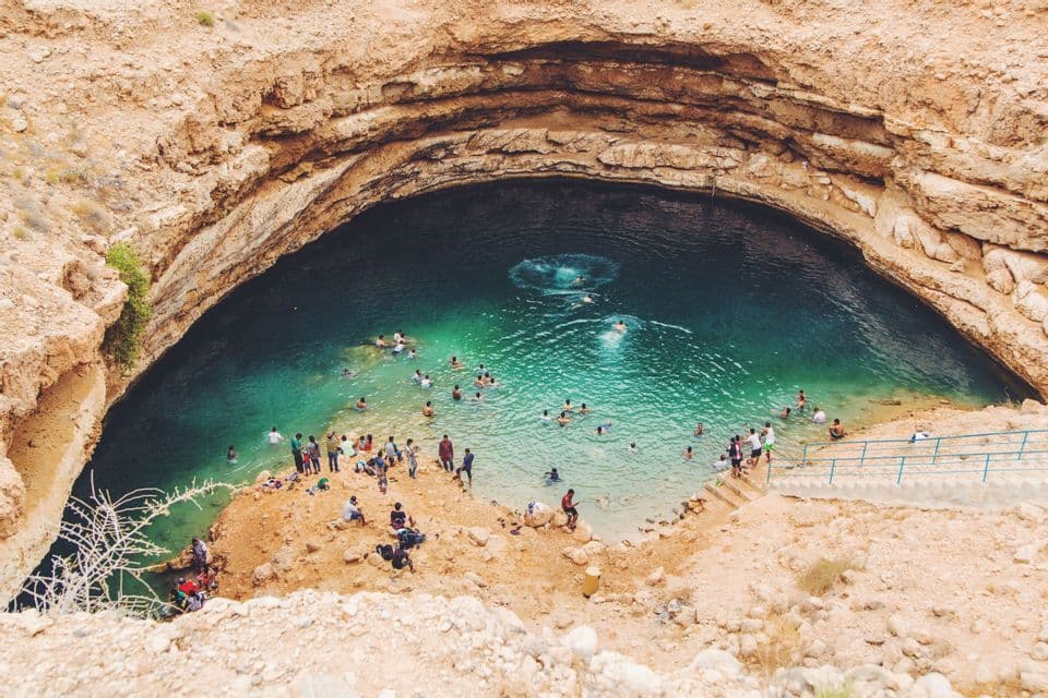 Ein Blick von oben auf viele Menschen, die im türkisfarbenen Wasser einer großen, felsigen Doline schwimmen und sich entspannen.