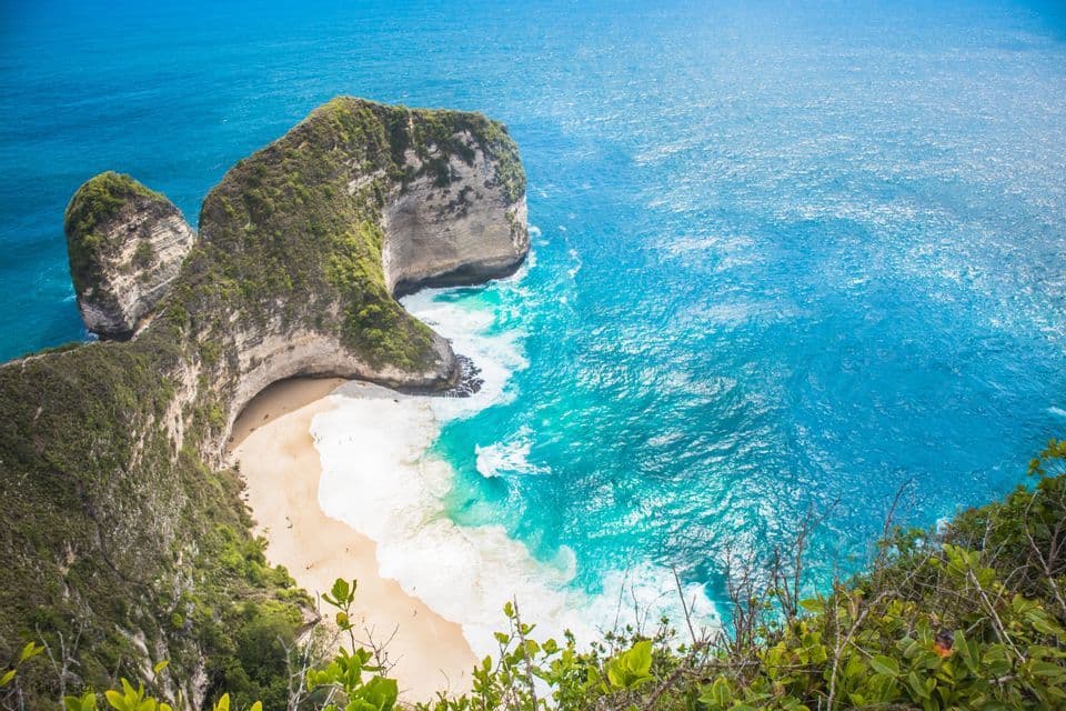 Una vista dall'alto di una scogliera ricoperta di verde che si protende in un oceano turchese, riparando una spiaggia isolata di sabbia bianca.