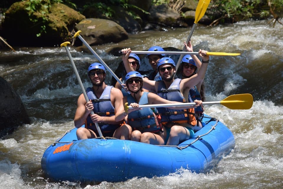 Un viaggio di gruppo WeRoad su un gommone blu naviga un fiume, con i membri che sorridono e alzano le pagaie.