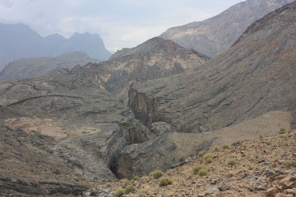 A panoramic view of a vast, rocky mountain range with a deep canyon cutting through the center under an overcast sky.