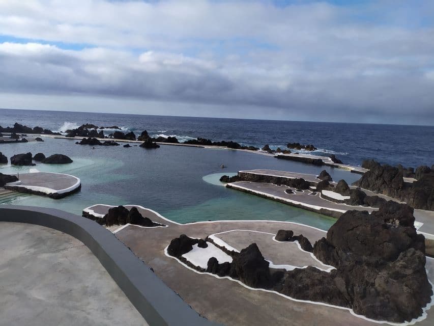 Piscine naturali costiere ricavate tra scure rocce vulcaniche, con l'oceano aperto sullo sfondo e un cielo nuvoloso.