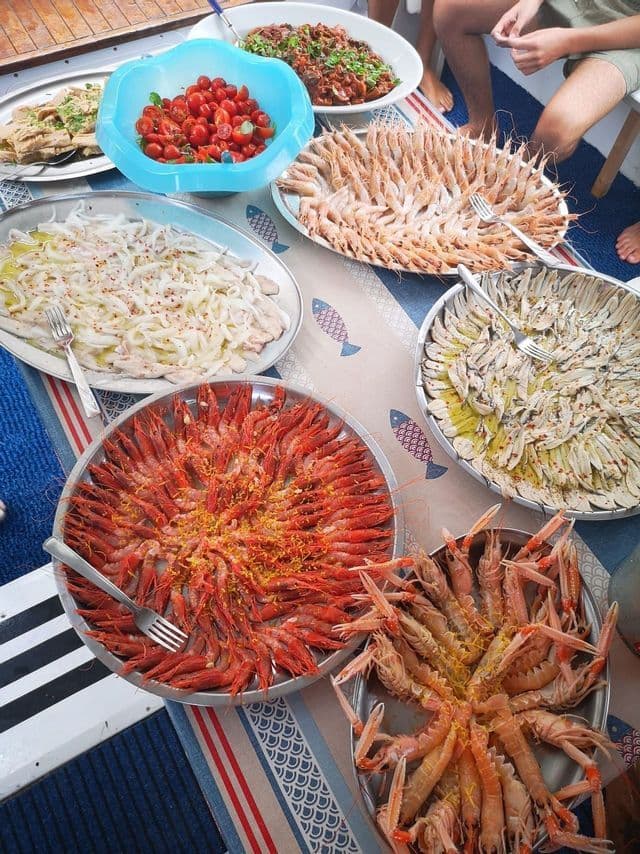 Una vista aérea de una mesa cargada con bandejas de mariscos frescos, incluyendo gambas rojas, cigalas y pescado marinado.