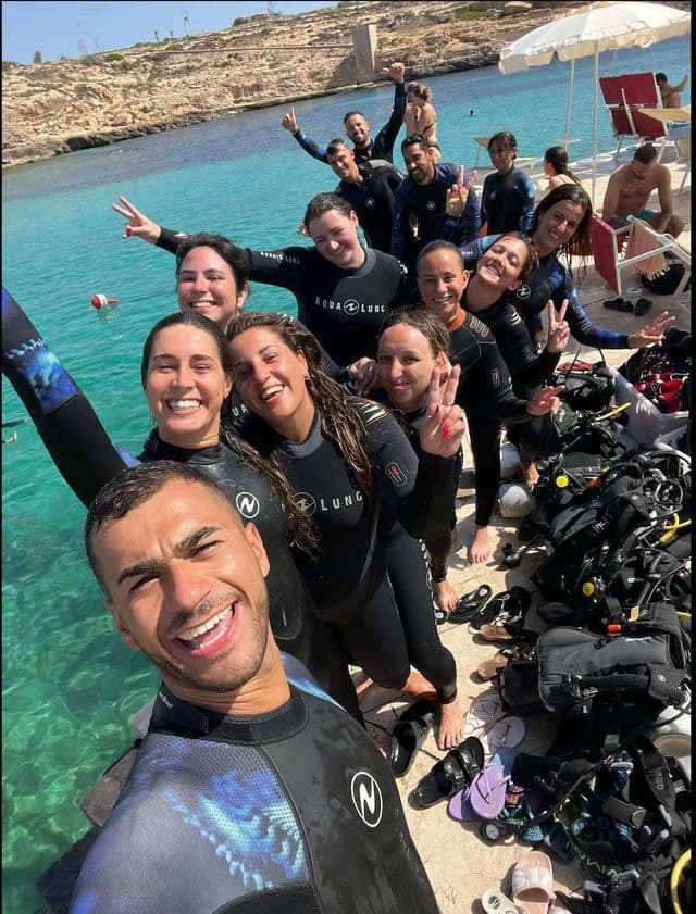 Un grupo de WeRoad en trajes de neopreno posa para una selfie en un muelle antes de una sesión de buceo.