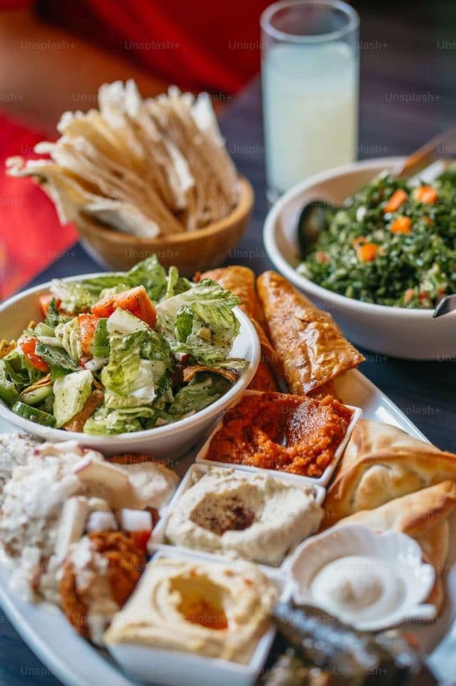 Un piatto di meze mediorientali con varie salse, insalate, pasticcini e pane piatto, disposti su un tavolo scuro.