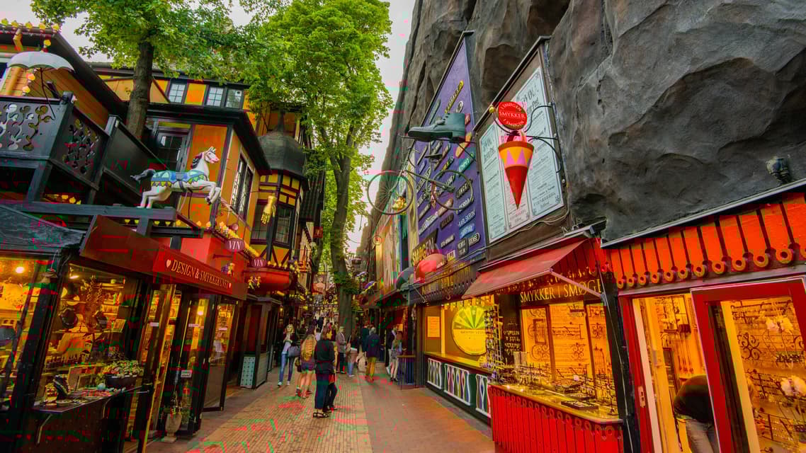 Personas paseando por una calle estrecha y pintoresca, con edificios coloridos y decorados y tiendas luminosas.
