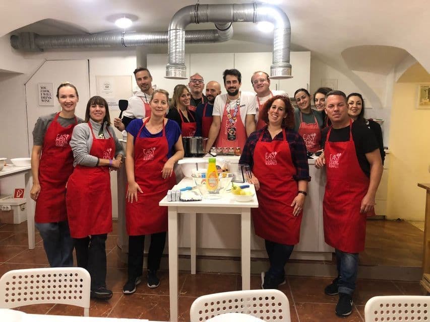 Eine WeRoad-Gruppe mit roten Schürzen lächelt für ein Gruppenfoto während eines Kochkurses in einer Küche.