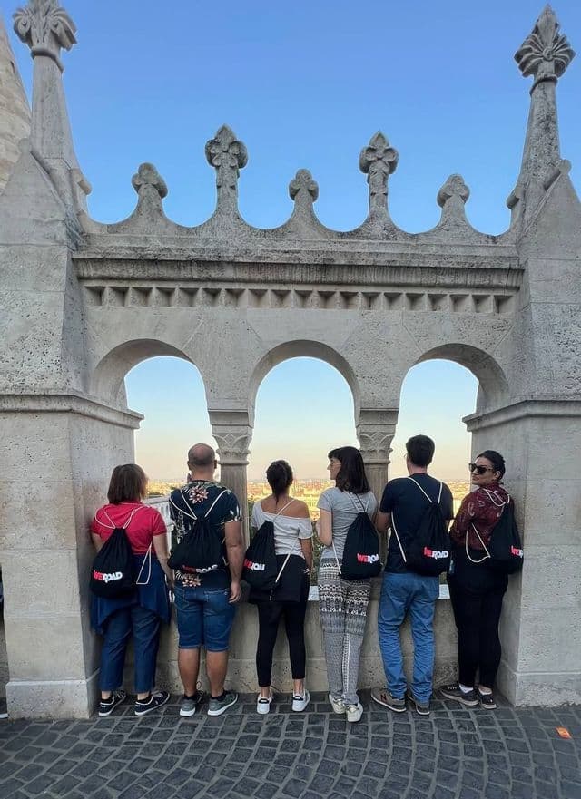 Eine WeRoad-Gruppe von hinten, die auf einem Steinbalkon mit Bögen steht und über eine Stadtlandschaft blickt.