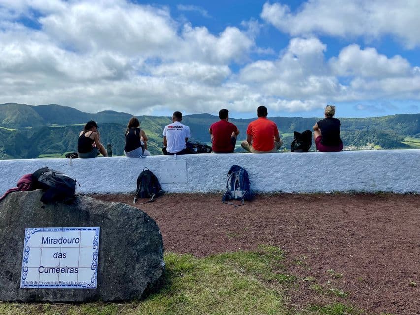 Un gruppo WeRoad seduto su un muro bianco, che osserva un paesaggio di colline verdi sotto un cielo nuvoloso.