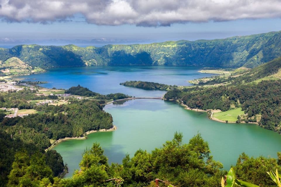 Una vista dall'alto di due laghi craterici collegati, uno blu e uno verde, incastonati tra pendii vulcanici lussureggianti e boscosi.