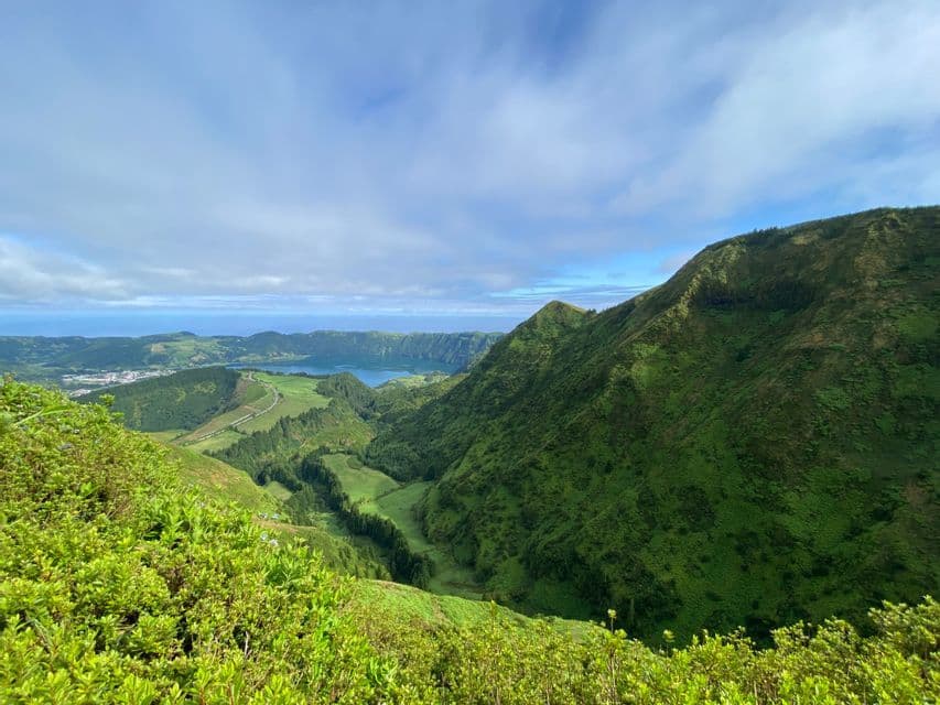 Una vista panoramica di verdi colline vulcaniche, un lago vulcanico in una valle e l'oceano all'orizzonte sotto un cielo nuvoloso.