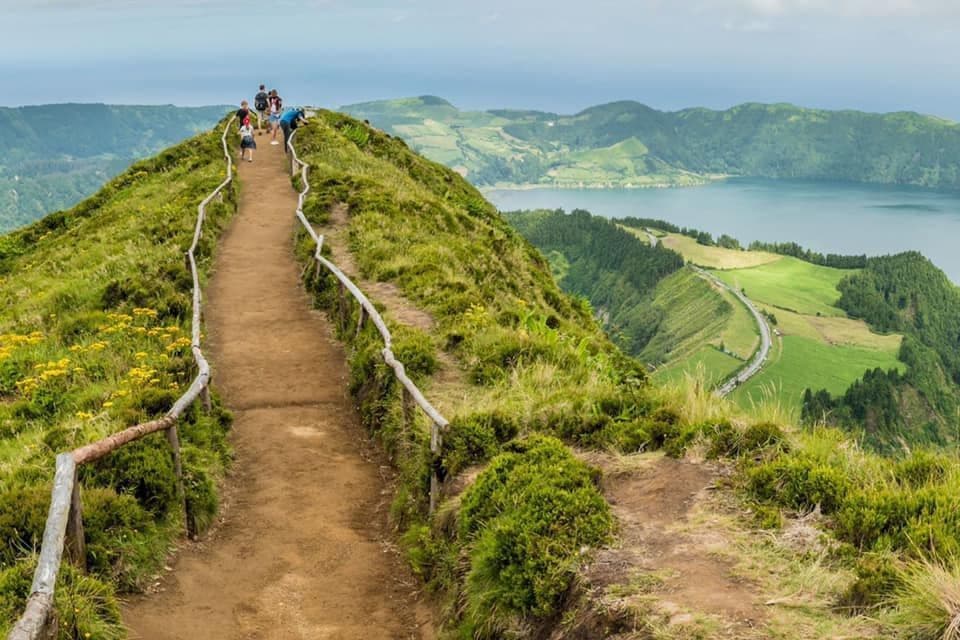 Un viaggio di gruppo WeRoad con escursione su uno stretto sentiero sterrato, lungo un crinale erboso che si affaccia su un vasto lago e verdi colline.