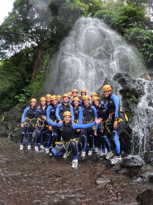 Un viaggio di gruppo WeRoad pronto per il canyoning, in posa con mute e caschi davanti a una cascata.