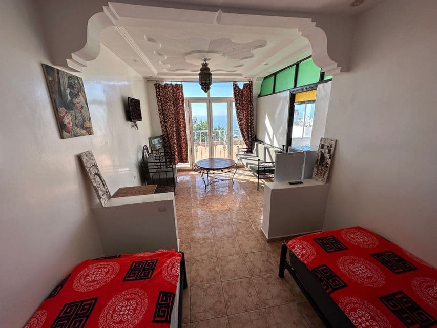 Interno di una camera su due livelli con due letti, un'area salotto e un balcone con vista sull'oceano.