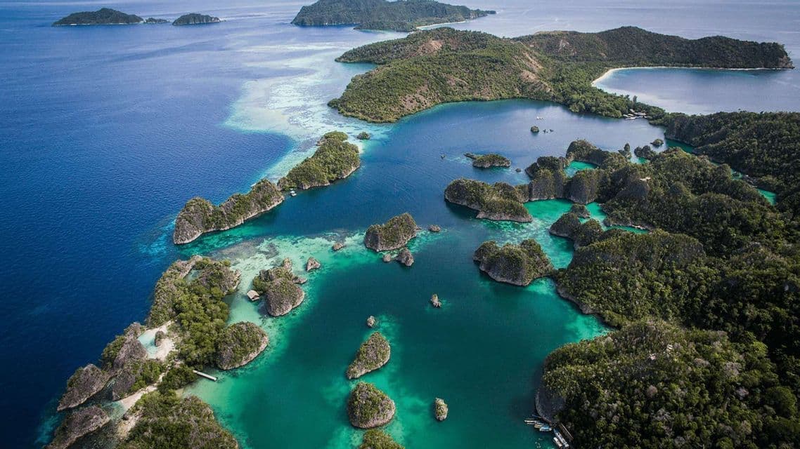 Una vista aérea de pequeñas islas rocosas cubiertas de árboles verdes, rodeadas de agua turquesa y azul profundo.