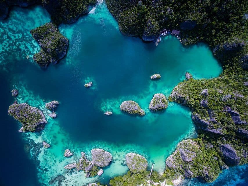 Vista aérea de un grupo de pequeñas islas verdes y rocosas en un mar tranquilo, turquesa y azul.