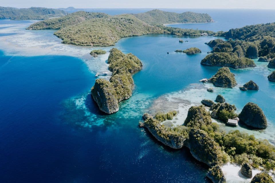 Una vista aérea de un archipiélago tropical con islas rocosas y verdes dispersas sobre agua turquesa y azul profundo.