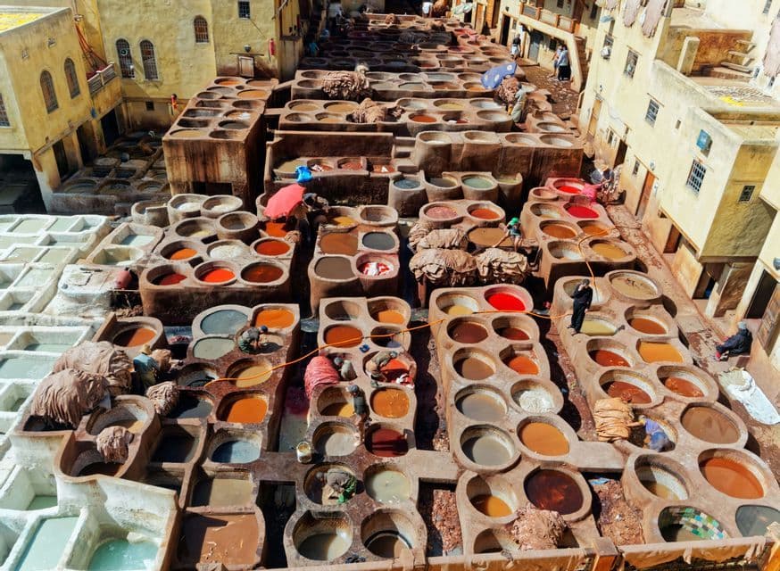 An aerial view of a traditional tannery with numerous stone vats filled with colorful dyes, where people are working.
