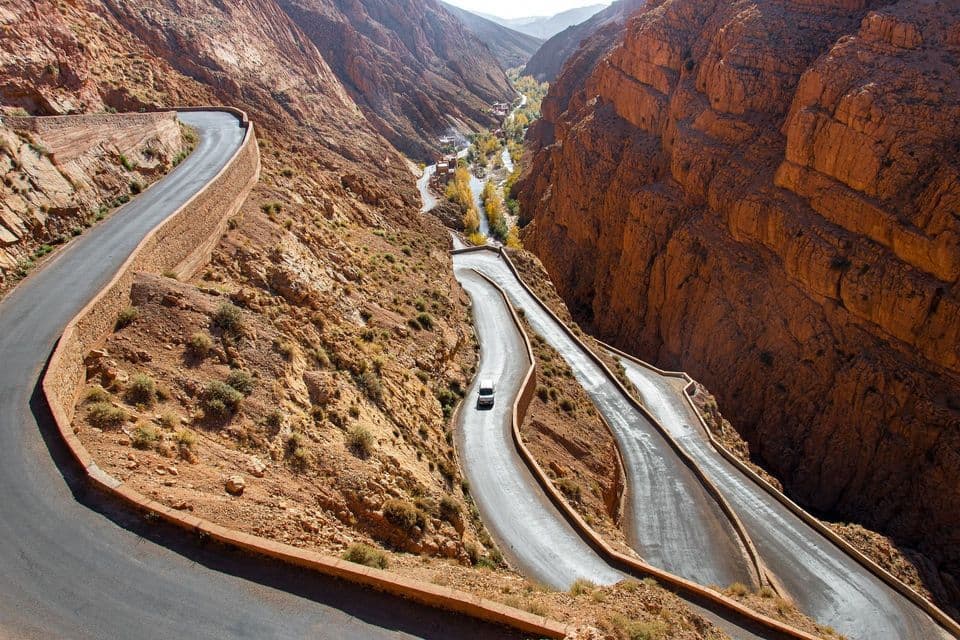 Una veduta dall'alto di un'auto bianca su una strada tortuosa con numerosi tornanti in un profondo canyon di roccia rossa.