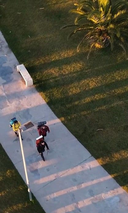 Vista aerea di un viaggio di gruppo WeRoad con tre persone, zaino in spalla, che camminano su un sentiero lastricato accanto a un'area erbosa.