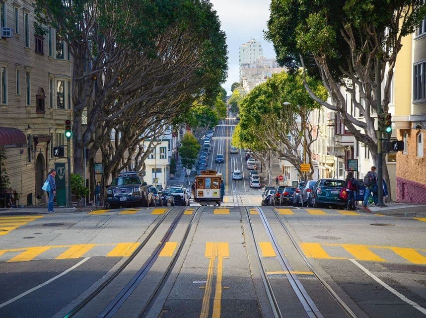 Un funiculaire monte une rue de ville escarpée et bordée d'arbres, avec des voitures garées le long des voies de tramway.