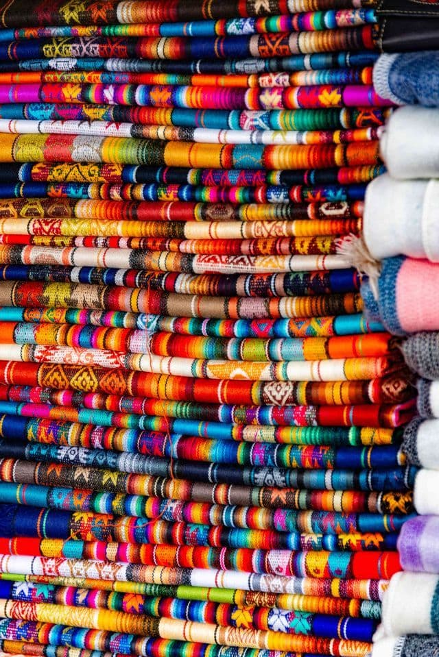Primer plano de una gran pila de textiles tejidos de colores con varios patrones y rayas.