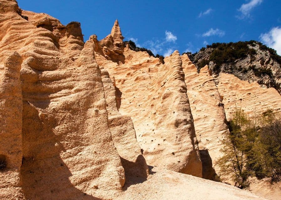 Formazioni rocciose frastagliate e dai toni arancioni, note come calanchi, si stagliano sotto un cielo blu intenso e una brillante luce solare.