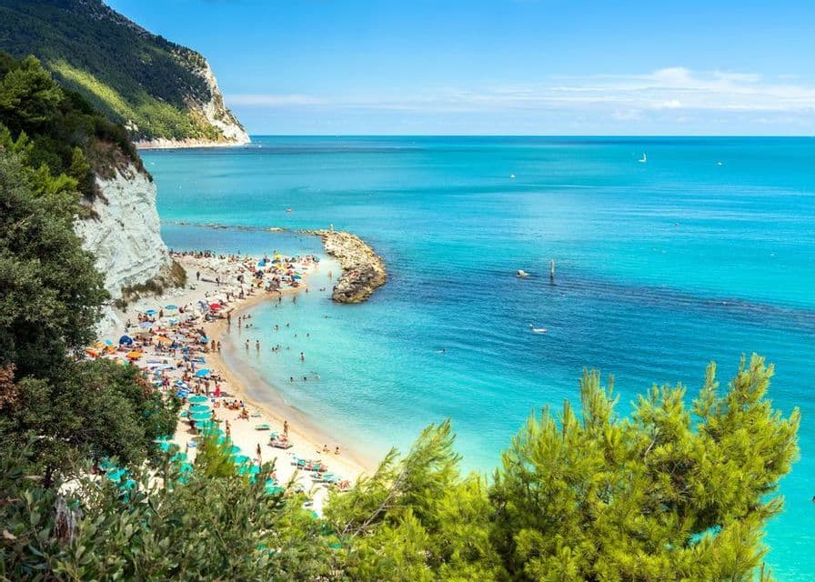 Una vista dall'alto di una spiaggia affollata con persone che nuotano in acqua turchese ai piedi di una scogliera bianca.