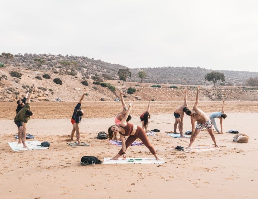 Un viaggio di gruppo WeRoad che pratica yoga su una spiaggia sabbiosa con colline sullo sfondo.