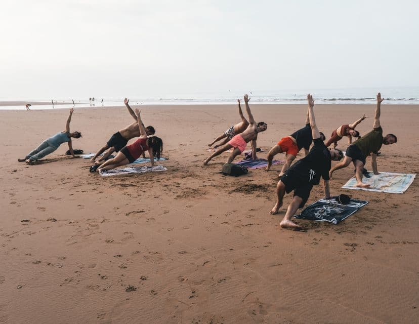 Un viaggio di gruppo WeRoad pratica yoga insieme su una spiaggia sabbiosa, mantenendo la posizione della plancia laterale all'unisono vicino all'oceano.