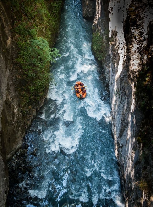 Vista aerea di un gruppo WeRoad che fa rafting su un gommone arancione, in un fiume impetuoso che attraversa un canyon profondo e stretto.
