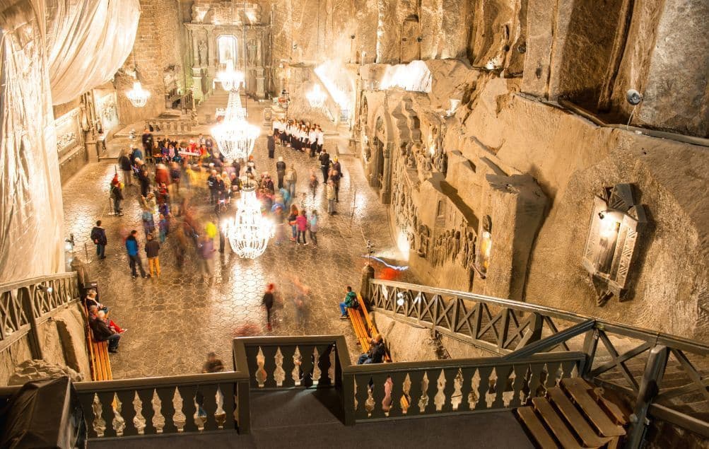 Eine von oben aufgenommene Langzeitbelichtung von Menschen in einer großen, aus Fels gehauenen Untergrundkapelle, beleuchtet von Kristalllüstern.