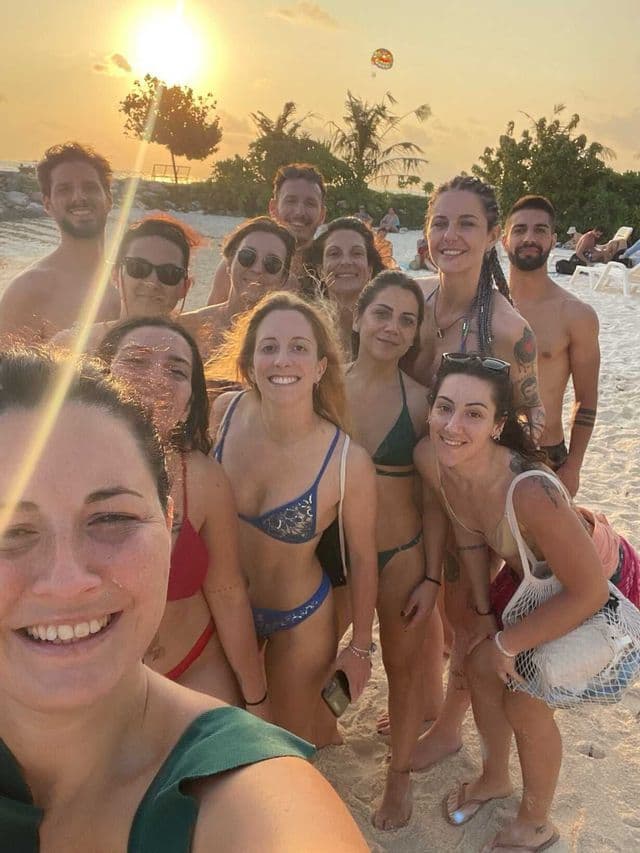A WeRoad group trip takes a smiling selfie together on a sandy beach at sunset.