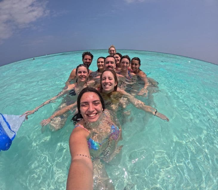 Eine WeRoad Gruppe macht ein lachendes Selfie beim Schwimmen im klaren, türkisen Meerwasser.