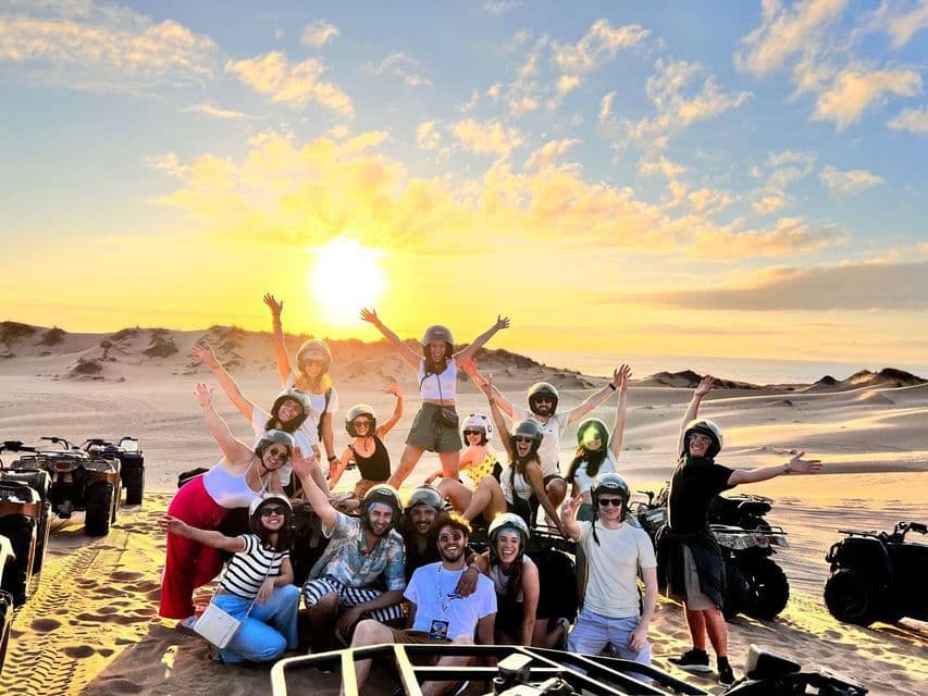 Un viaggio di gruppo WeRoad sorride e posa con i quad sulle dune di sabbia al tramonto.