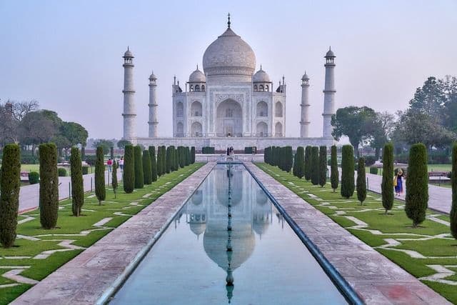 El Taj Mahal se alza al final de un largo estanque reflectante, flanqueado simétricamente por jardines y cipreses.