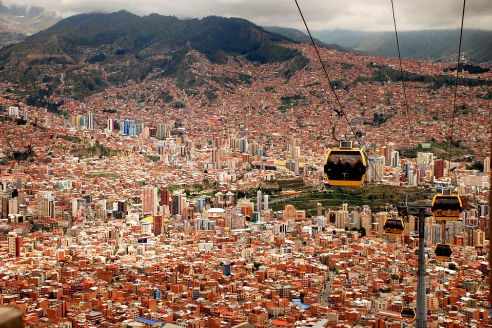 Vista aérea de teleféricos amarillos viajando sobre una ciudad densamente poblada con edificios de tejados de terracota a la base de una gran montaña.
