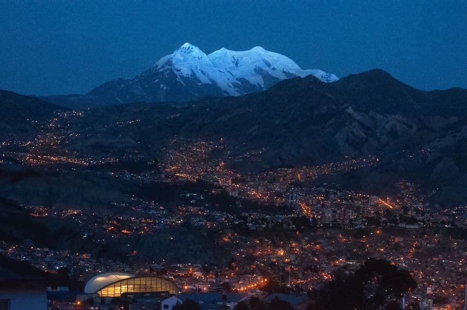 Una cordillera nevada domina una ciudad iluminada enclavada en un valle al anochecer.
