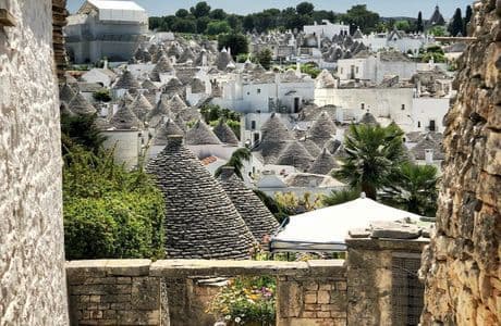 A village of whitewashed Trulli houses with conical stone roofs viewed from a high vantage point between stone walls.