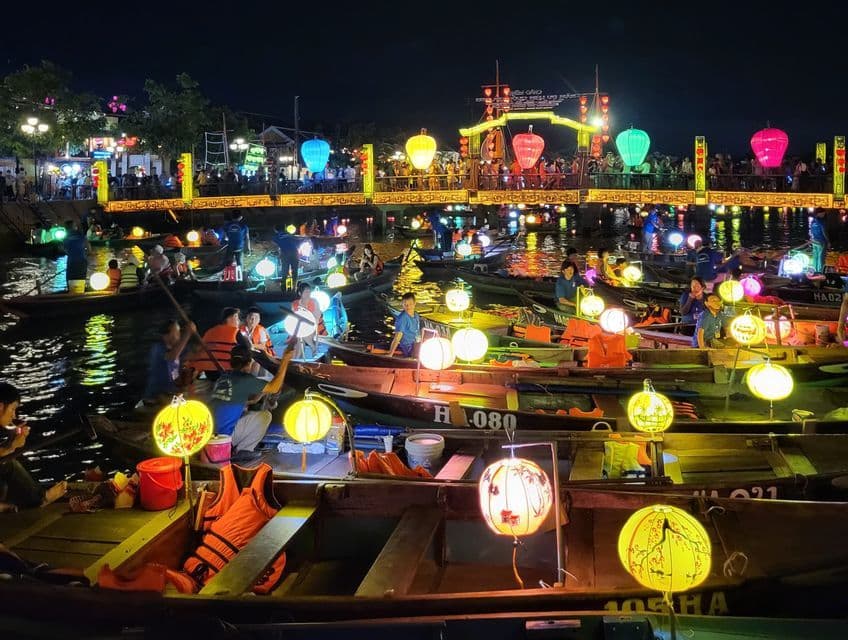 Un viaje en grupo de WeRoad en pequeños barcos por un río de noche, iluminado por coloridas linternas de papel durante un festival.