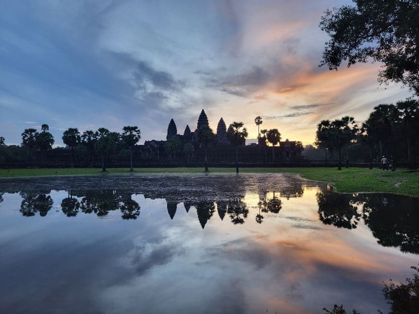 La silueta del templo de Angkor Wat y las palmeras reflejadas en un lago tranquilo durante un amanecer colorido.