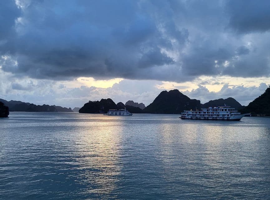 Dos cruceros surcan las aguas entre karsts rocosos bajo un cielo nublado al atardecer.