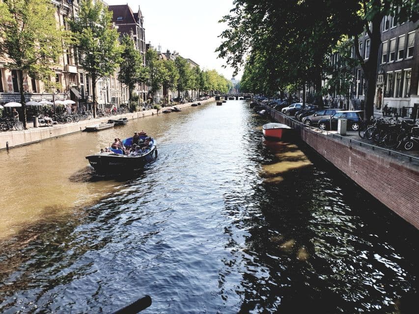 Un viaje en grupo de WeRoad en un barco turístico recorre un canal urbano flanqueado por árboles y edificios históricos.